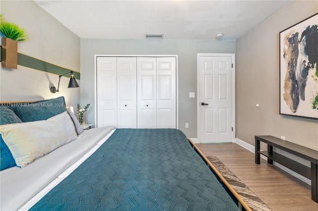 bedroom with baseboards, wood finished floors, visible vents, and a closet