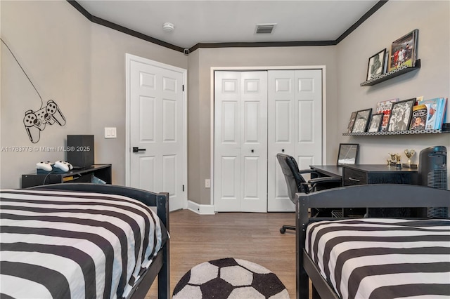 bedroom featuring baseboards, visible vents, wood finished floors, a closet, and ornamental molding