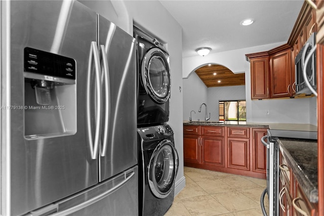 laundry area featuring stacked washer and dryer, arched walkways, a sink, light tile patterned flooring, and laundry area