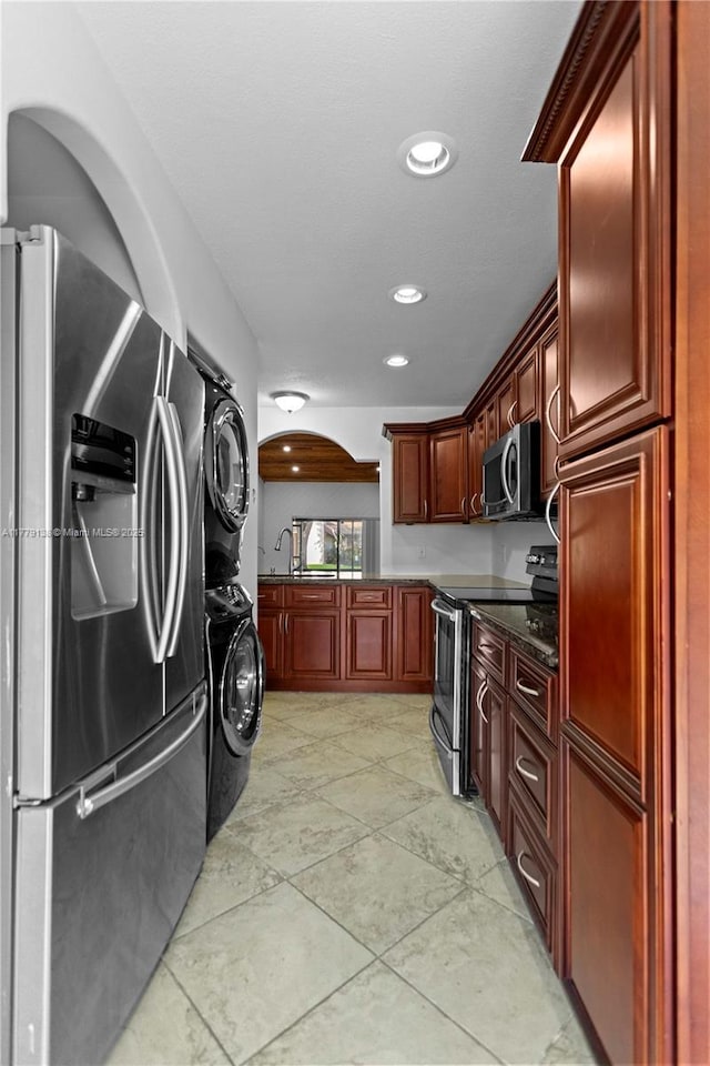 kitchen with stacked washer and dryer, stainless steel appliances, arched walkways, recessed lighting, and reddish brown cabinets