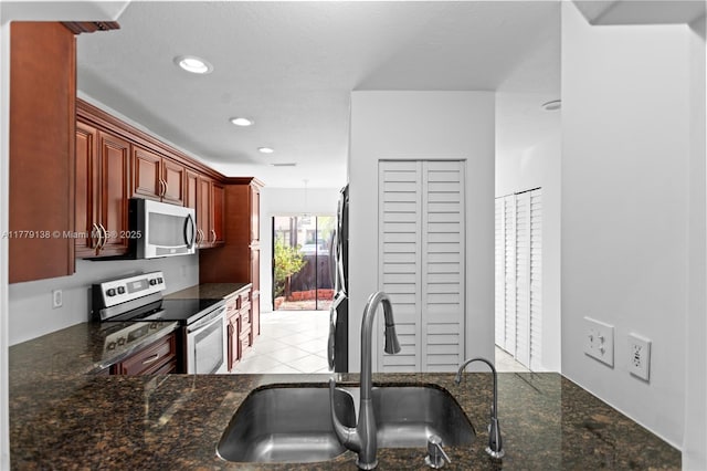 kitchen with recessed lighting, stainless steel appliances, dark brown cabinets, a sink, and dark stone counters