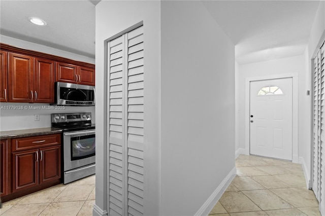 kitchen with dark countertops, recessed lighting, appliances with stainless steel finishes, reddish brown cabinets, and light tile patterned floors