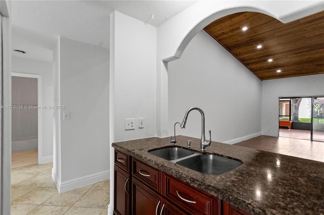 kitchen featuring a sink, dark stone counters, dark brown cabinets, lofted ceiling, and wooden ceiling