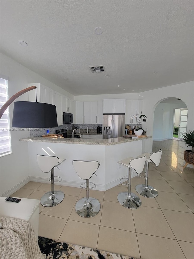 3708 NE 22nd Pl, Homestead, FL 33033 - kitchen featuring stainless steel fridge with ice dispenser, white cabinets, visible vents, arched walkways, and black microwave