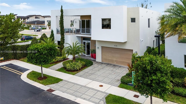 contemporary home with an attached garage, a balcony, decorative driveway, and stucco siding