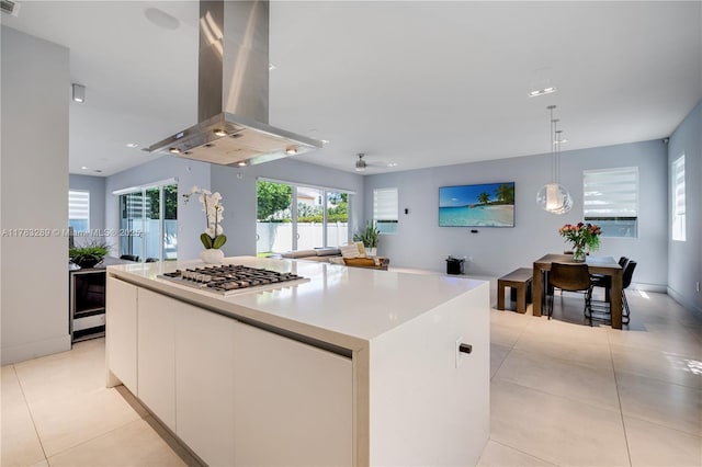 kitchen with light tile patterned floors, white cabinets, stainless steel gas stovetop, island exhaust hood, and a kitchen island