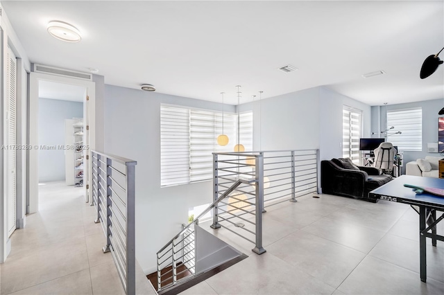 hallway featuring visible vents, tile patterned floors, and an upstairs landing