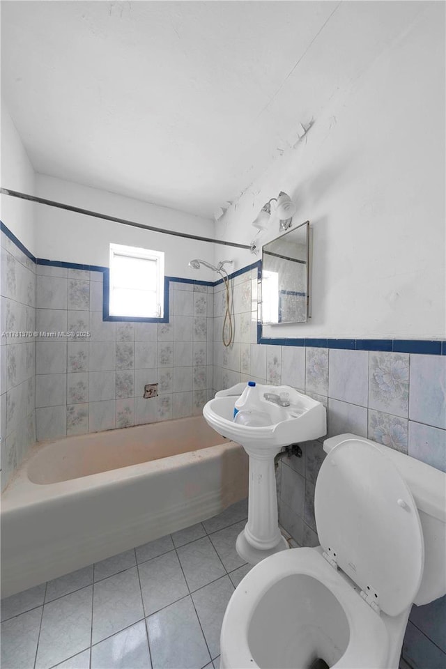 full bath with bathing tub / shower combination, tile patterned flooring, toilet, wainscoting, and tile walls