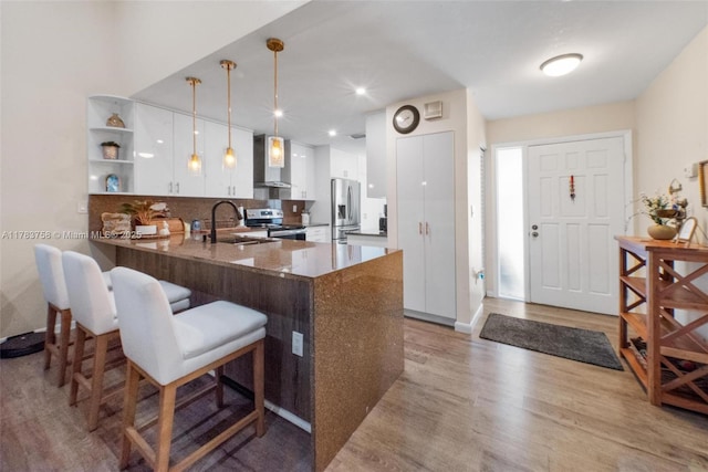 9909 NW 52nd Ln, Doral, FL 33178 - kitchen with stainless steel appliances, a peninsula, wall chimney exhaust hood, white cabinetry, and light wood-style floors