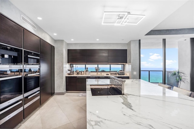 18555 Collins Ave Unit 5505, Sunny Isles Beach, FL 33160 - kitchen with modern cabinets, light stone countertops, black electric cooktop, dark brown cabinetry, and recessed lighting