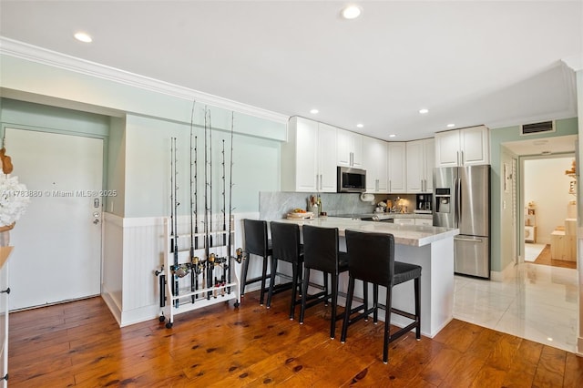 kitchen with visible vents, a peninsula, crown molding, white cabinetry, and stainless steel appliances