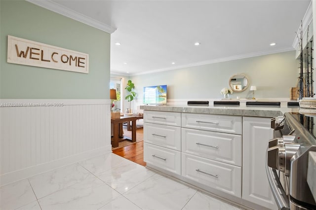 kitchen featuring ornamental molding, white cabinets, marble finish floor, wainscoting, and stainless steel range