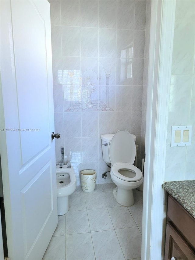 half bath with toilet, tile walls, a bidet, vanity, and tile patterned flooring