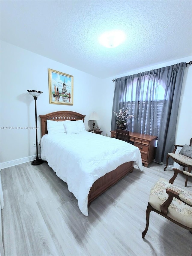 bedroom featuring light wood-style flooring, a textured ceiling, and baseboards