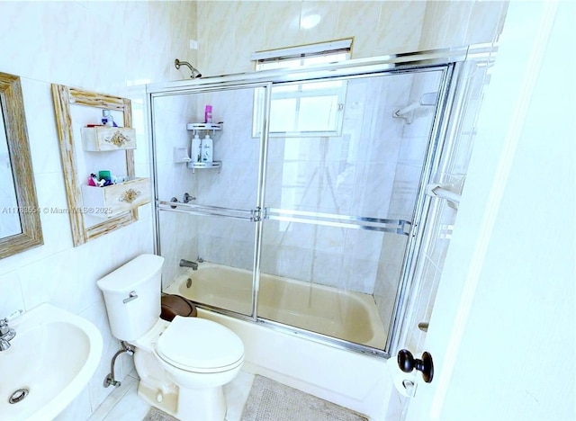 full bath featuring combined bath / shower with glass door, tile walls, a sink, and toilet