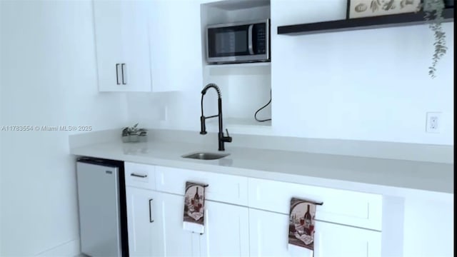 kitchen with stainless steel microwave, light countertops, white cabinetry, dishwashing machine, and a sink