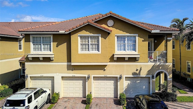 multi unit property with an attached garage, a tiled roof, driveway, and stucco siding