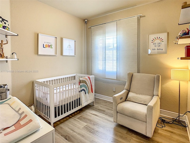bedroom featuring a closet, baseboards, a nursery area, and wood finished floors