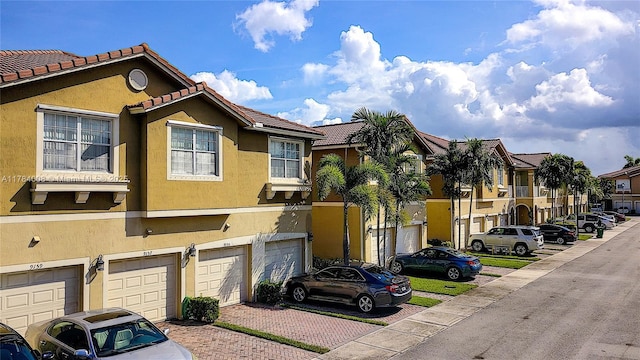 view of front of house featuring a tiled roof, a garage, stucco siding, a residential view, and driveway