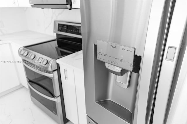 interior space with white cabinetry, light stone counters, marble finish floor, range with two ovens, and fridge