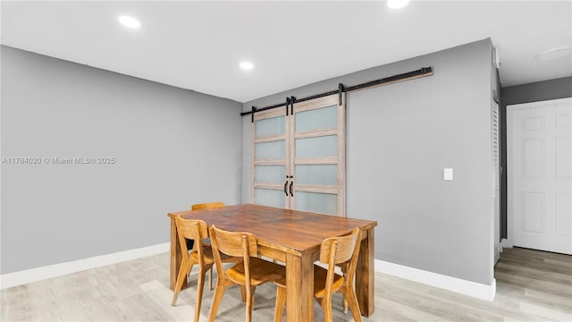dining space with baseboards, a barn door, light wood-style floors, and recessed lighting