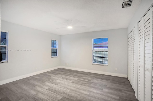 unfurnished bedroom featuring wood finished floors, baseboards, multiple windows, and visible vents
