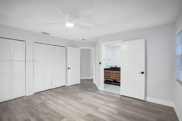 unfurnished bedroom with visible vents, baseboards, multiple closets, and wood finished floors