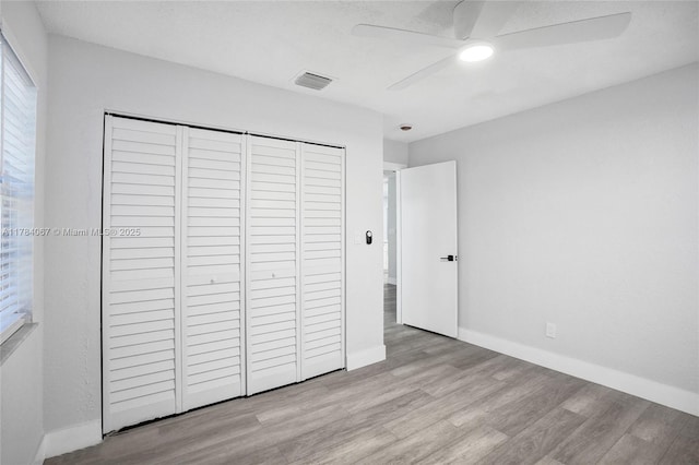 unfurnished bedroom featuring ceiling fan, a closet, visible vents, wood finished floors, and baseboards