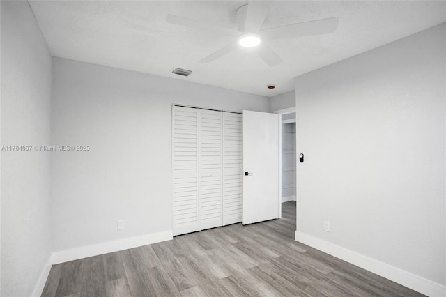 unfurnished bedroom featuring a closet, baseboards, visible vents, ceiling fan, and wood finished floors