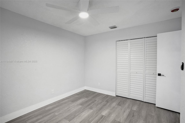unfurnished bedroom featuring a closet, baseboards, a ceiling fan, visible vents, and wood finished floors