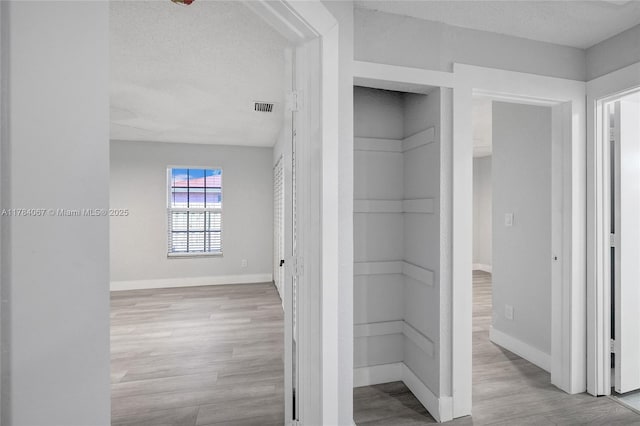corridor featuring a textured ceiling, wood finished floors, baseboards, and visible vents