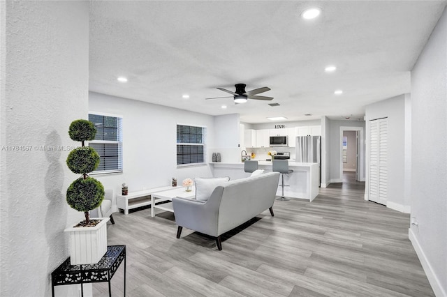 living area with recessed lighting, ceiling fan, light wood finished floors, and baseboards