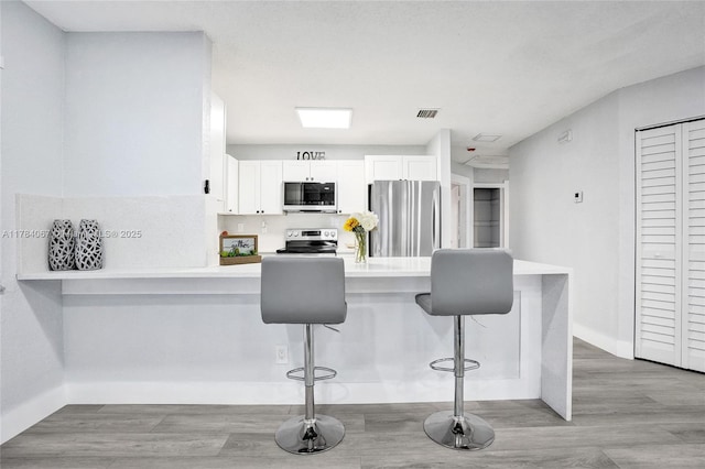 kitchen with stainless steel appliances, light wood-style floors, white cabinets, and a kitchen breakfast bar