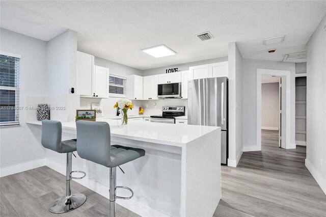 kitchen with white cabinets, visible vents, light countertops, stainless steel appliances, and a breakfast bar area