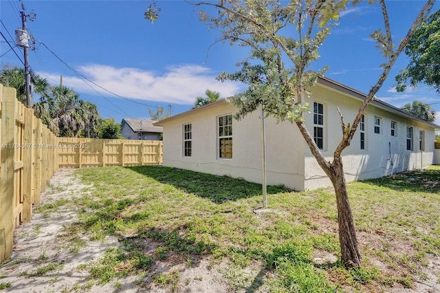 view of side of home with a yard, stucco siding, and fence