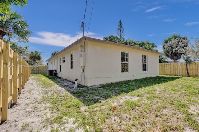view of side of home with stucco siding, a fenced backyard, a lawn, and central AC