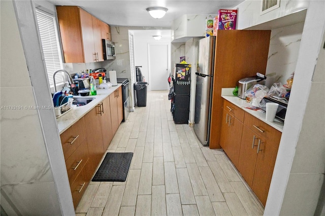 kitchen with visible vents, a sink, light countertops, brown cabinetry, and stainless steel appliances