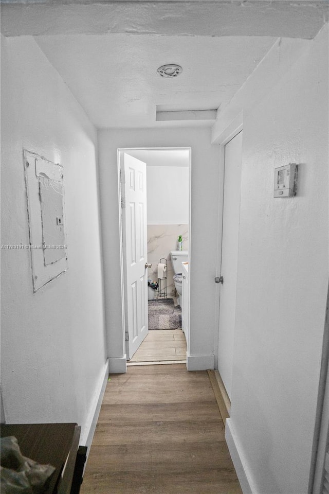 corridor with electric panel, baseboards, and wood finished floors