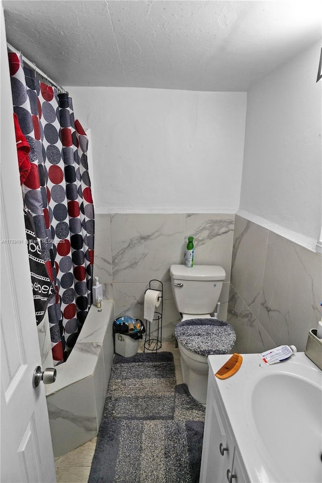 bathroom with toilet, tile walls, a textured ceiling, vanity, and a wainscoted wall