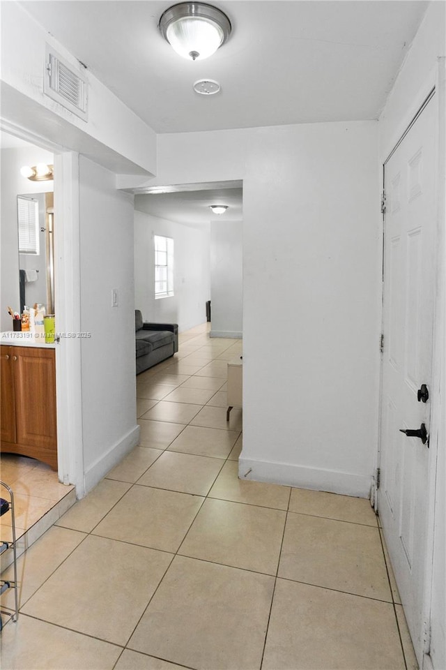 hall featuring visible vents, baseboards, and light tile patterned floors