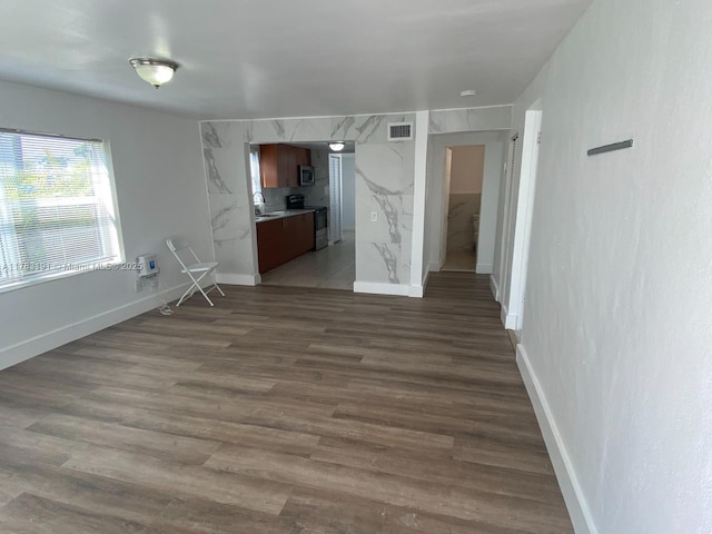 unfurnished living room featuring visible vents, baseboards, a sink, and dark wood finished floors