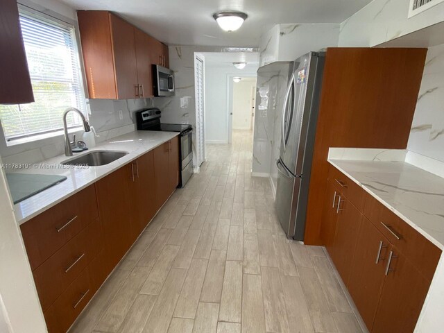 kitchen featuring light wood-style flooring, visible vents, a sink, stainless steel appliances, and brown cabinets