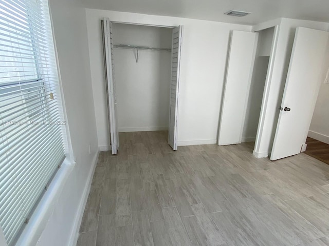 unfurnished bedroom featuring light wood-style floors, visible vents, baseboards, and a closet
