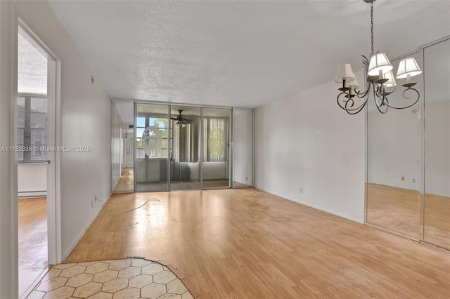 unfurnished room with a wealth of natural light, baseboard heating, a chandelier, and wood finished floors