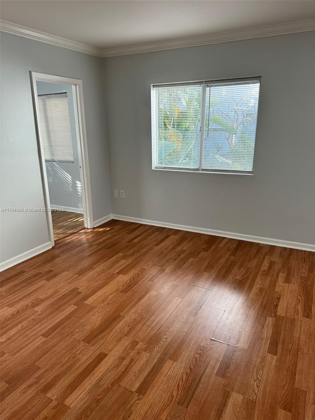 empty room with crown molding, wood finished floors, and baseboards