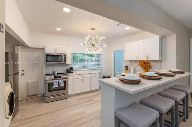 3313 SE 3rd St, Pompano Beach, FL 33062 - kitchen with appliances with stainless steel finishes, washer / clothes dryer, white cabinets, a kitchen breakfast bar, and recessed lighting