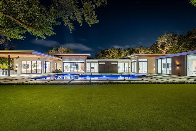 back of house at twilight featuring a lawn and an outdoor pool