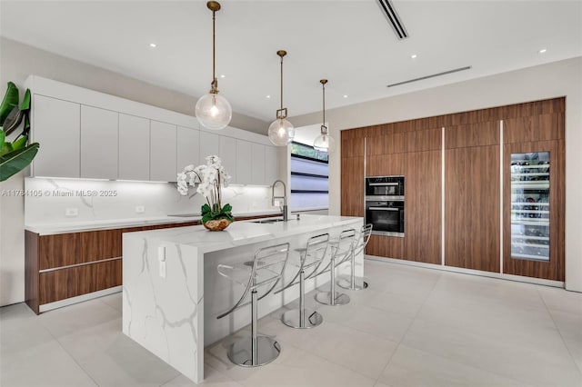 kitchen with wall oven, brown cabinetry, modern cabinets, a sink, and recessed lighting