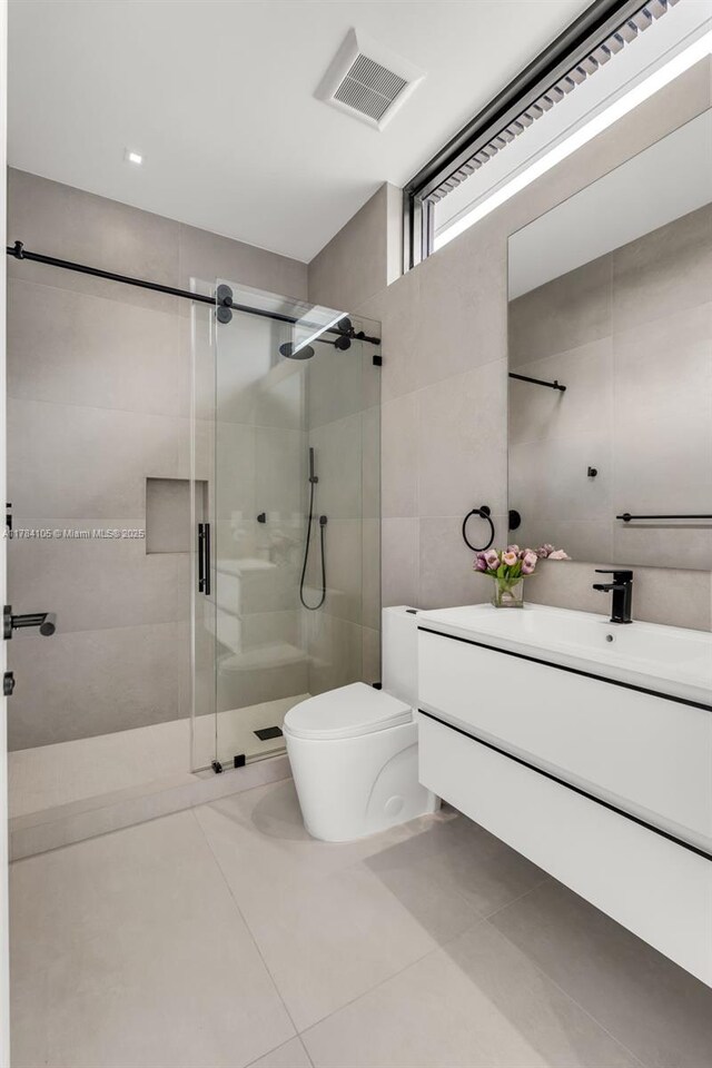 full bath featuring a shower stall, tile patterned floors, toilet, vanity, and tile walls