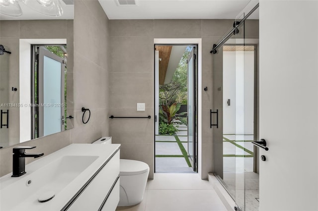 bathroom with tile walls, a stall shower, tile patterned flooring, vanity, and toilet